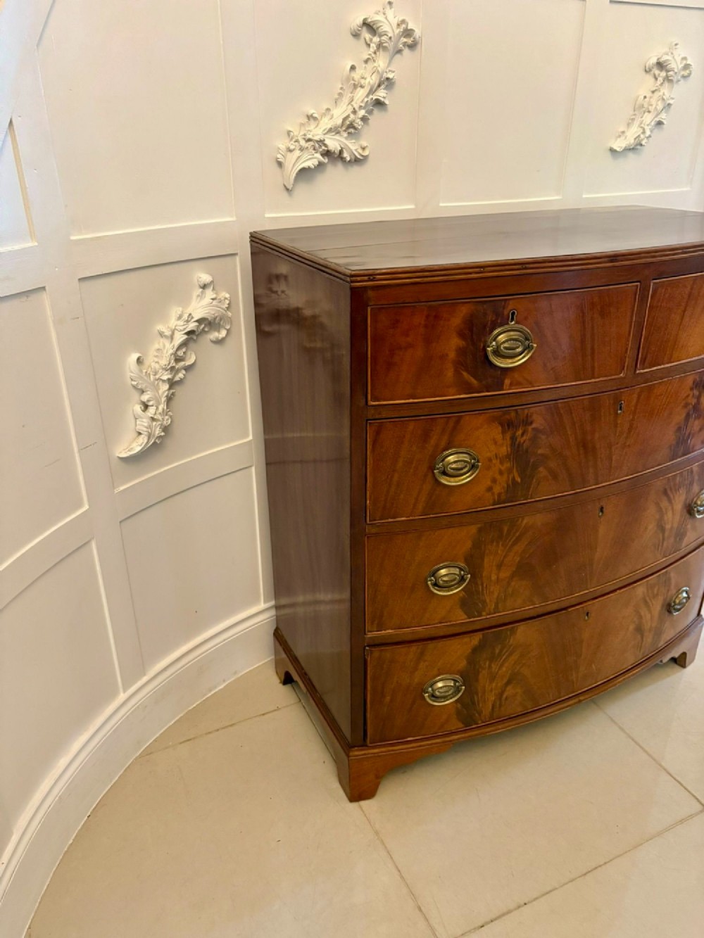 A George III mahogany bowfront chest of drawers featuring two short drawers over three long drawers with oval brass handles and splayed bracket feet. View IV