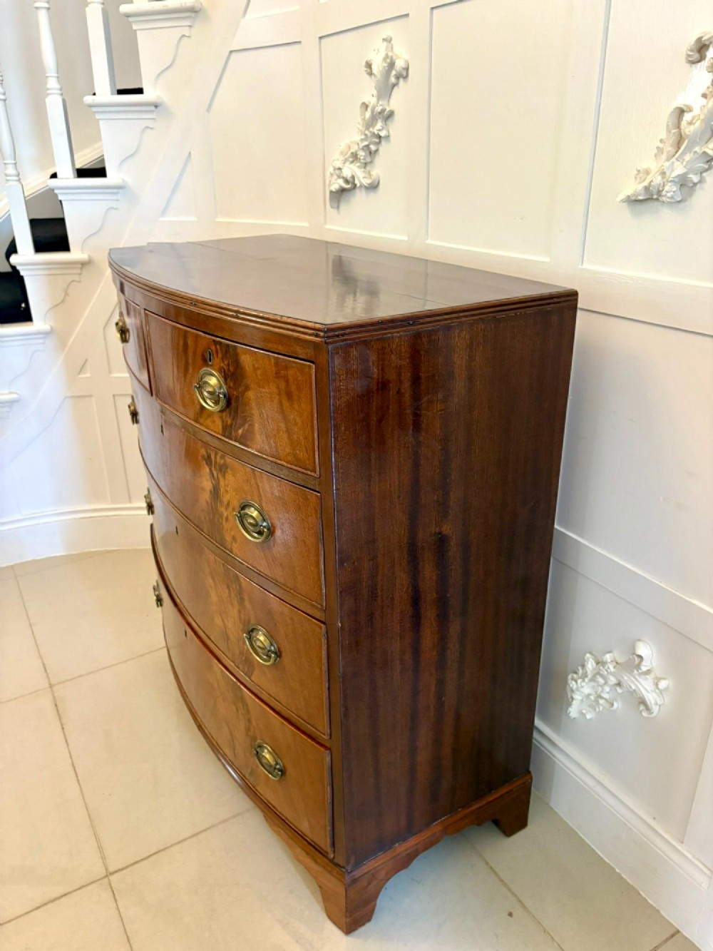 A George III mahogany bowfront chest of drawers featuring two short drawers over three long drawers with oval brass handles and splayed bracket feet. View V