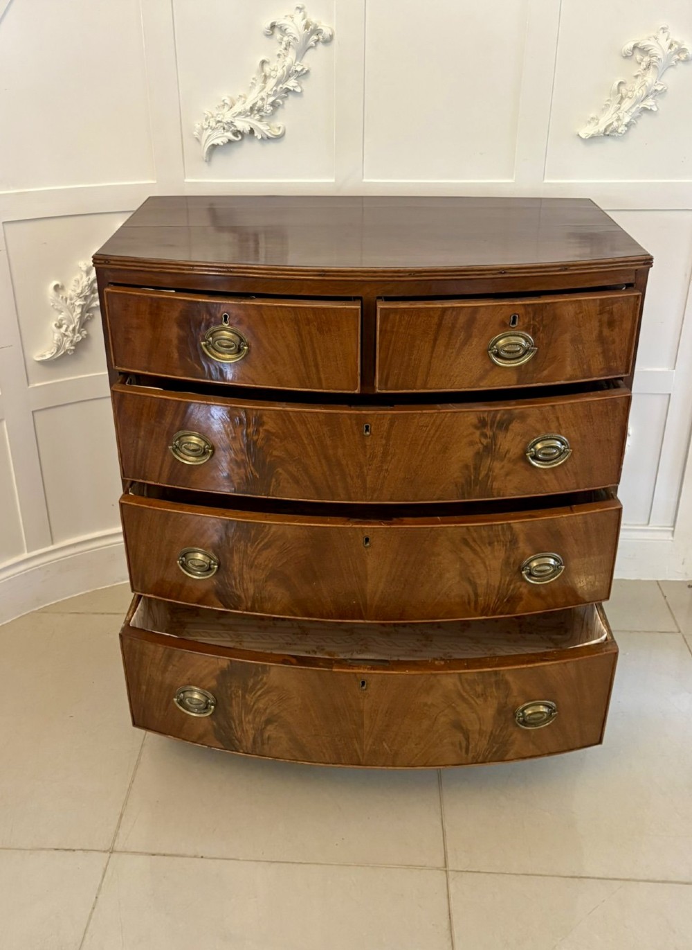 A George III mahogany bowfront chest of drawers featuring two short drawers over three long drawers with oval brass handles and splayed bracket feet. View VI