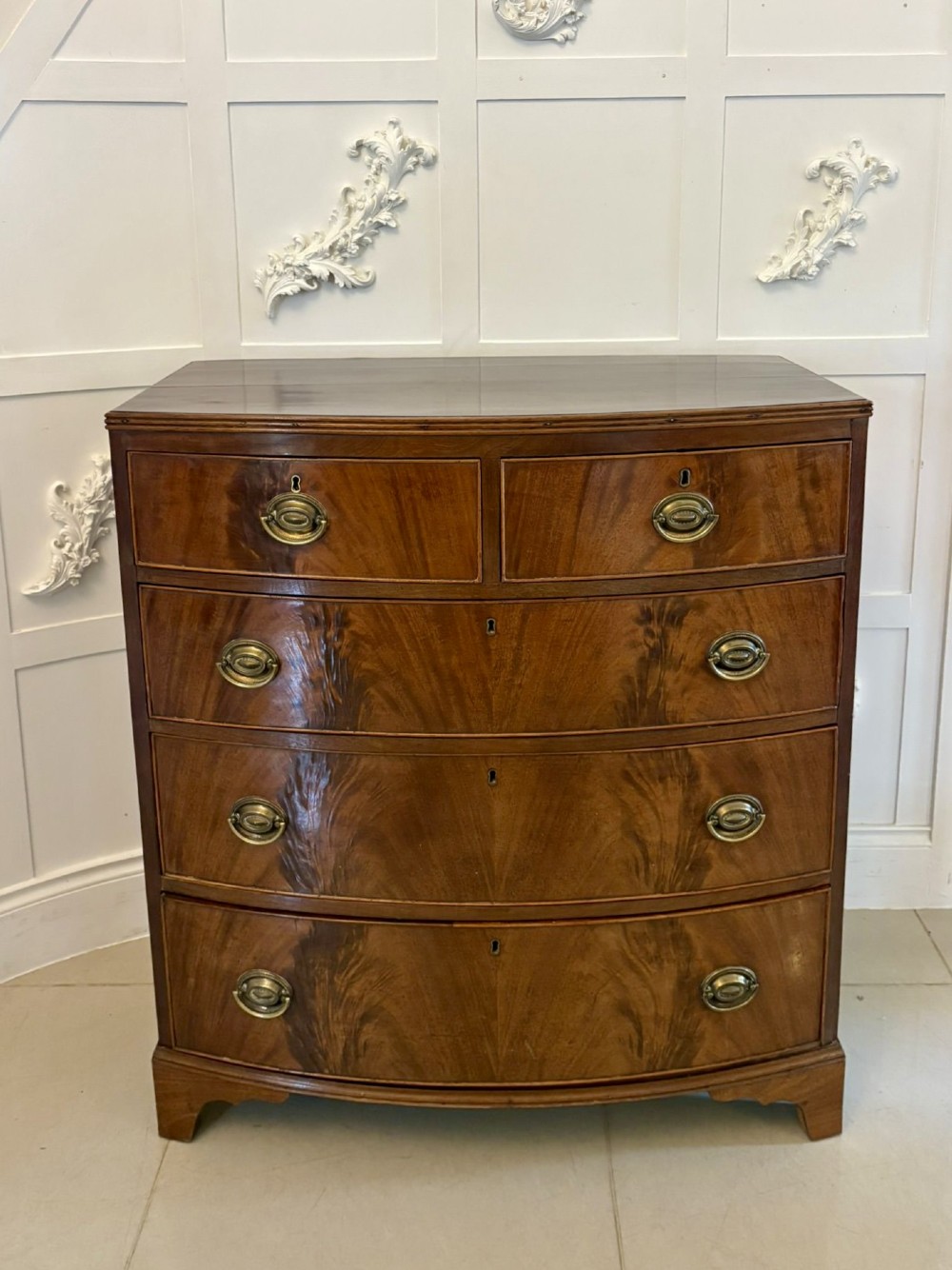 A George III mahogany bowfront chest of drawers featuring two short drawers over three long drawers with oval brass handles and splayed bracket feet.