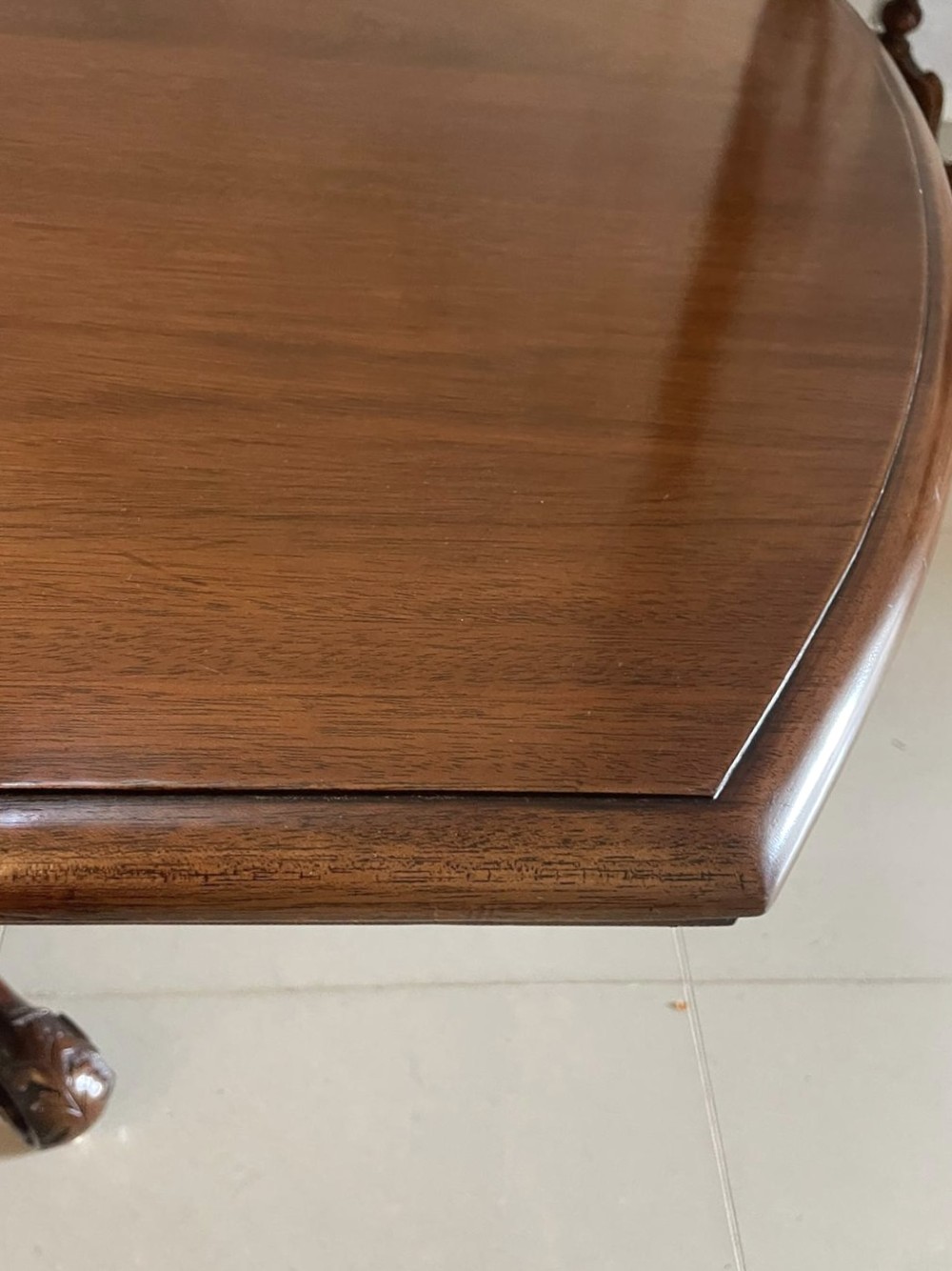 A Victorian mahogany tilt-top dining table with a polished flame mahogany surface shown tilted vertically on a carved pedestal tripod base with castors. View II