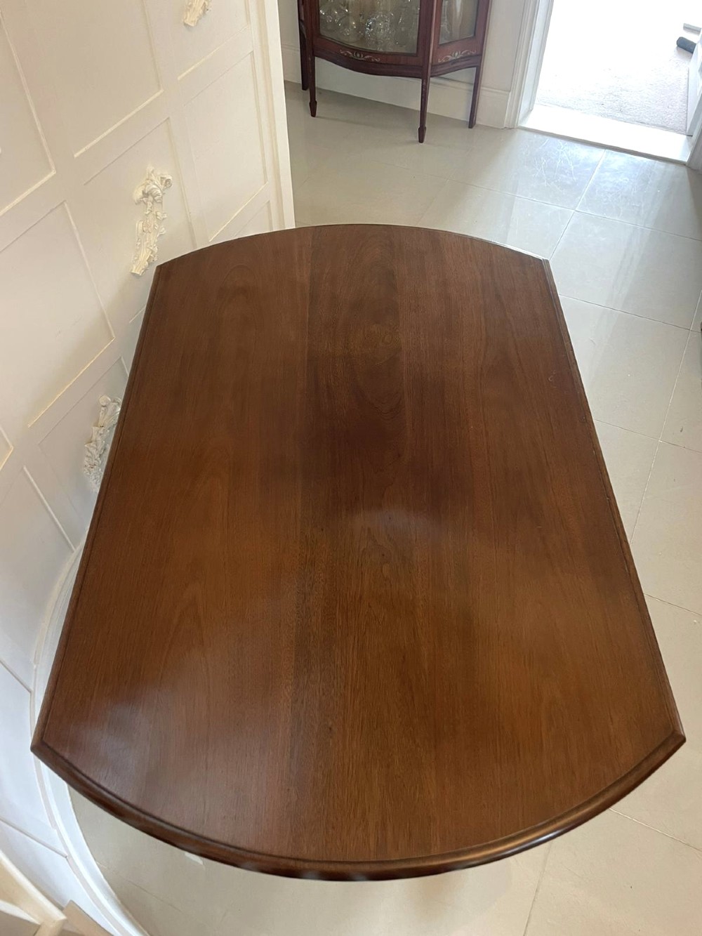 A Victorian mahogany tilt-top dining table with a polished flame mahogany surface shown tilted vertically on a carved pedestal tripod base with castors. View III
