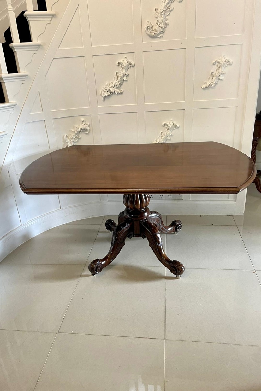 A Victorian mahogany tilt-top dining table with a polished flame mahogany surface shown tilted vertically on a carved pedestal tripod base with castors. View IV