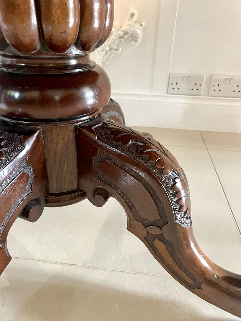A Victorian mahogany tilt-top dining table with a polished flame mahogany surface shown tilted vertically on a carved pedestal tripod base with castors. View V