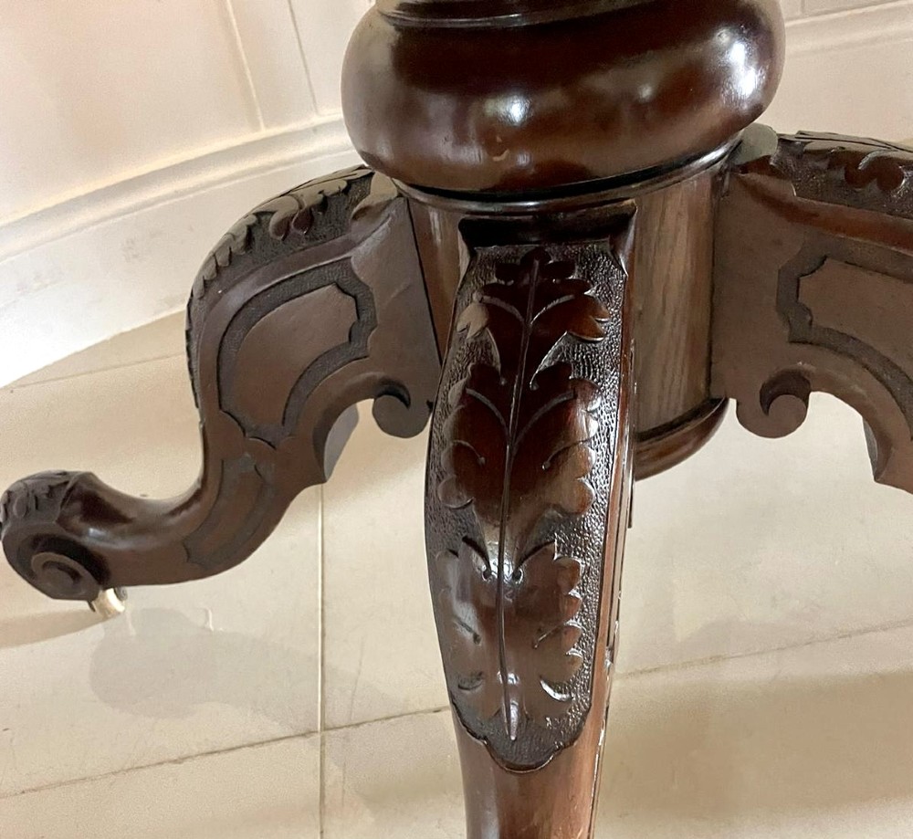 A Victorian mahogany tilt-top dining table with a polished flame mahogany surface shown tilted vertically on a carved pedestal tripod base with castors. View VII