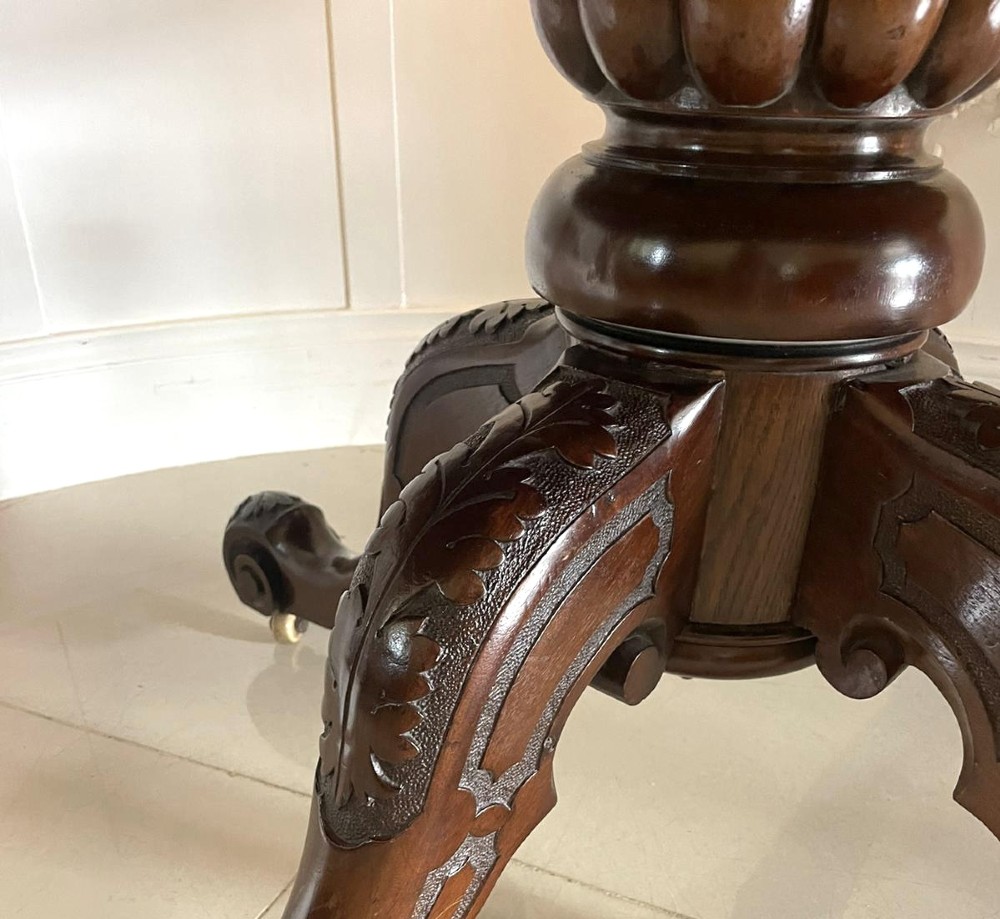 A Victorian mahogany tilt-top dining table with a polished flame mahogany surface shown tilted vertically on a carved pedestal tripod base with castors. View VIII