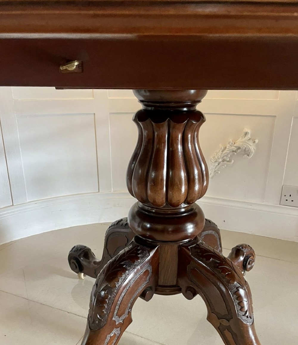 A Victorian mahogany tilt-top dining table with a polished flame mahogany surface shown tilted vertically on a carved pedestal tripod base with castors. View IX