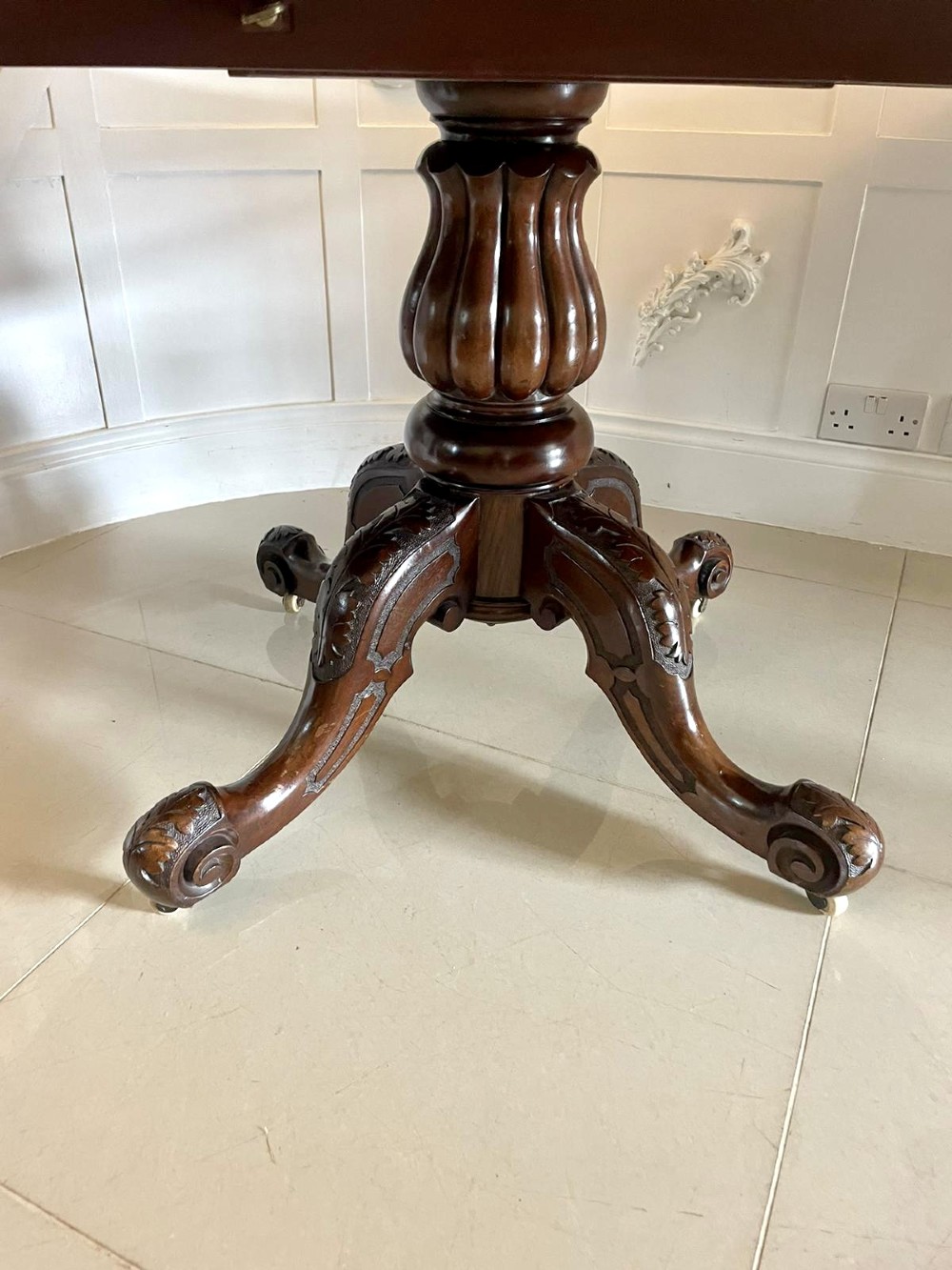 A Victorian mahogany tilt-top dining table with a polished flame mahogany surface shown tilted vertically on a carved pedestal tripod base with castors. View X