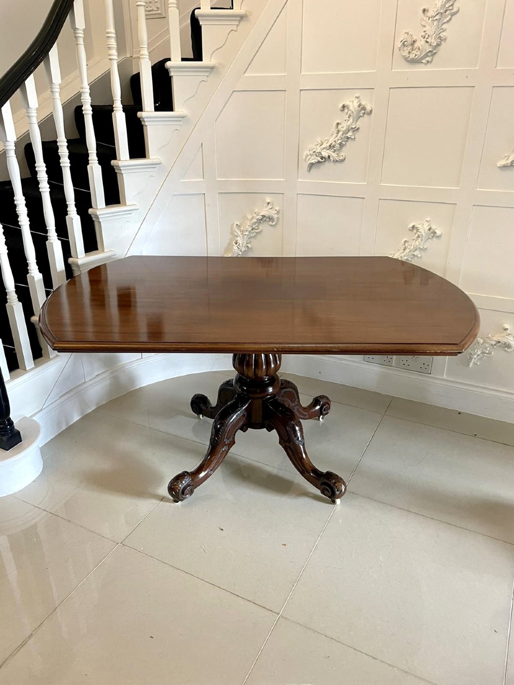 A Victorian mahogany tilt-top dining table with a polished flame mahogany surface shown tilted vertically on a carved pedestal tripod base with castors. View XI