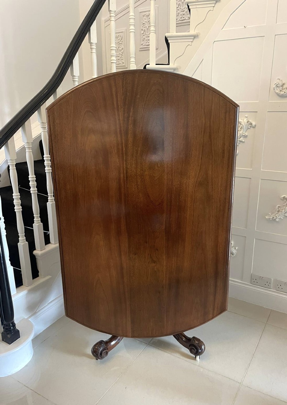 A Victorian mahogany tilt-top dining table with a polished flame mahogany surface shown tilted vertically on a carved pedestal tripod base with castors.