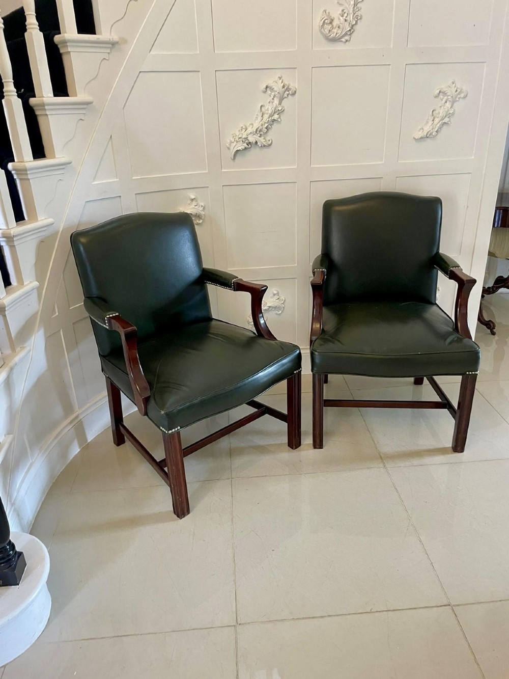A pair of dark green leather armchairs with polished mahogany frames and brass stud detailing along the upholstery edges. View V