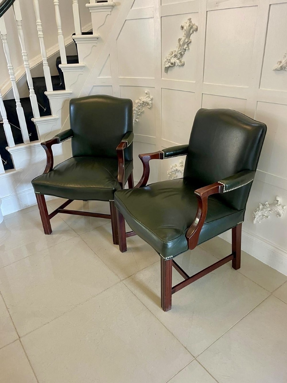 A pair of dark green leather armchairs with polished mahogany frames and brass stud detailing along the upholstery edges. View VI