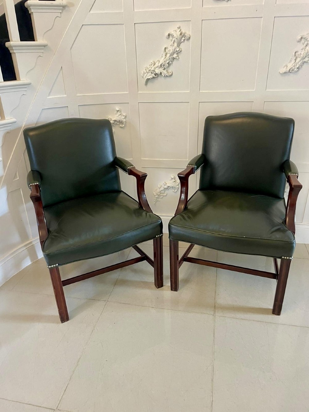 A pair of dark green leather armchairs with polished mahogany frames and brass stud detailing along the upholstery edges. View VII