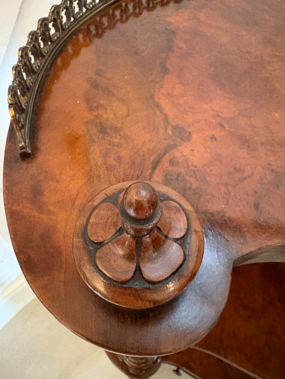 A Victorian burr walnut three-tier serpentine-shaped whatnot featuring turned corner supports, a pierced brass gallery rim, a single bottom drawer, and brass castors. View II