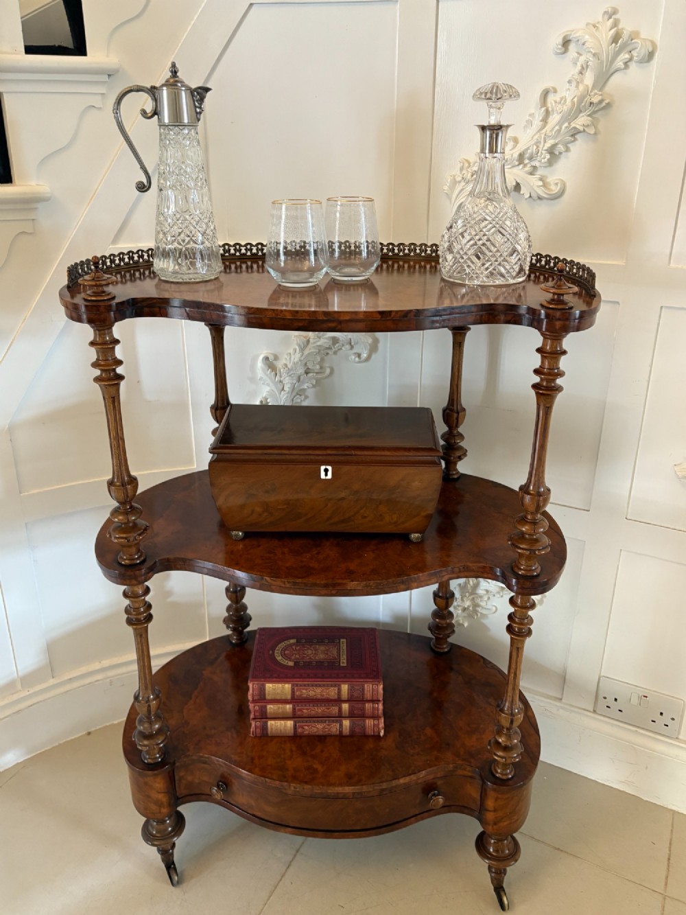 A Victorian burr walnut three-tier serpentine-shaped whatnot featuring turned corner supports, a pierced brass gallery rim, a single bottom drawer, and brass castors. View III