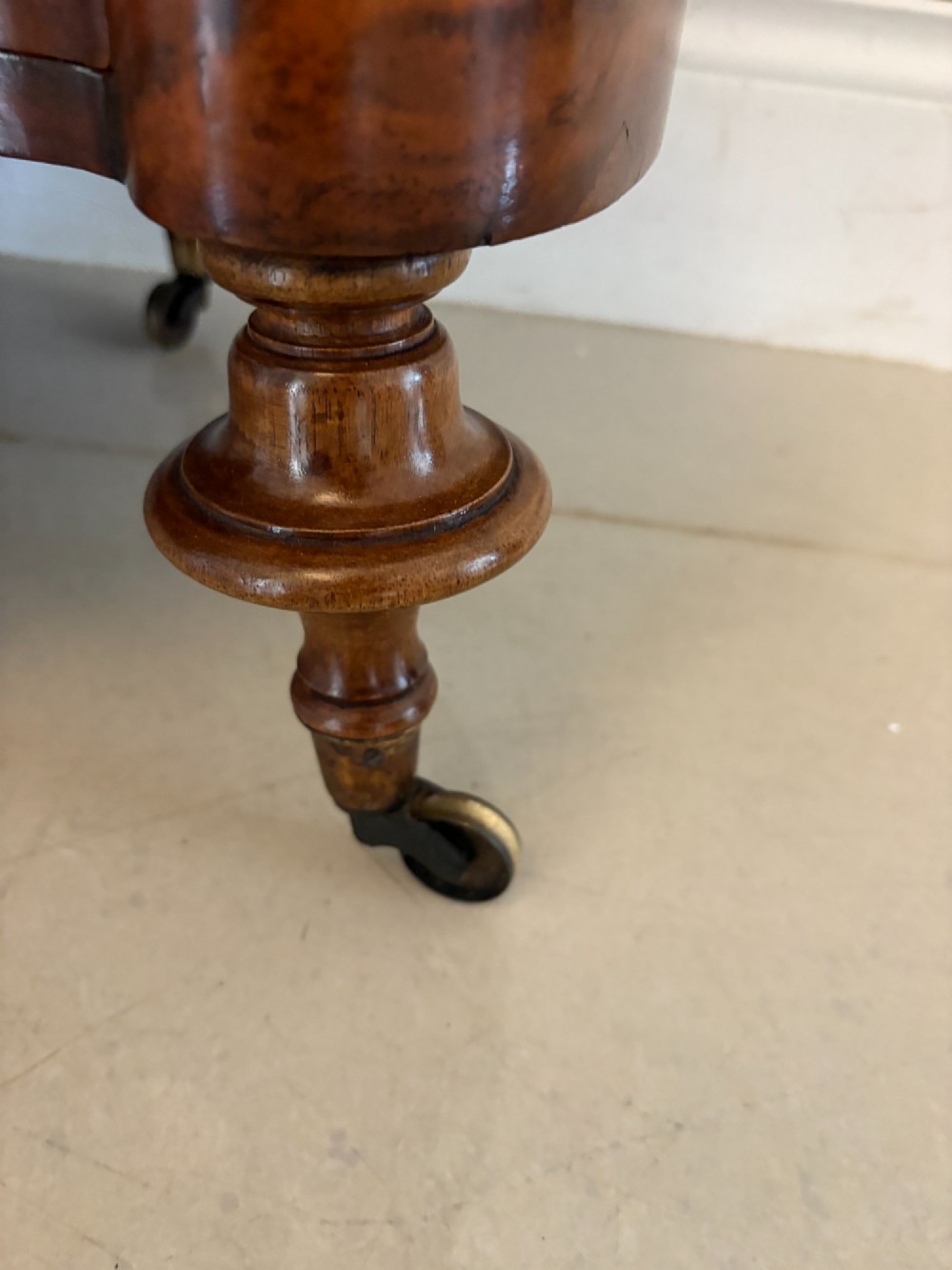 A Victorian burr walnut three-tier serpentine-shaped whatnot featuring turned corner supports, a pierced brass gallery rim, a single bottom drawer, and brass castors. View IX