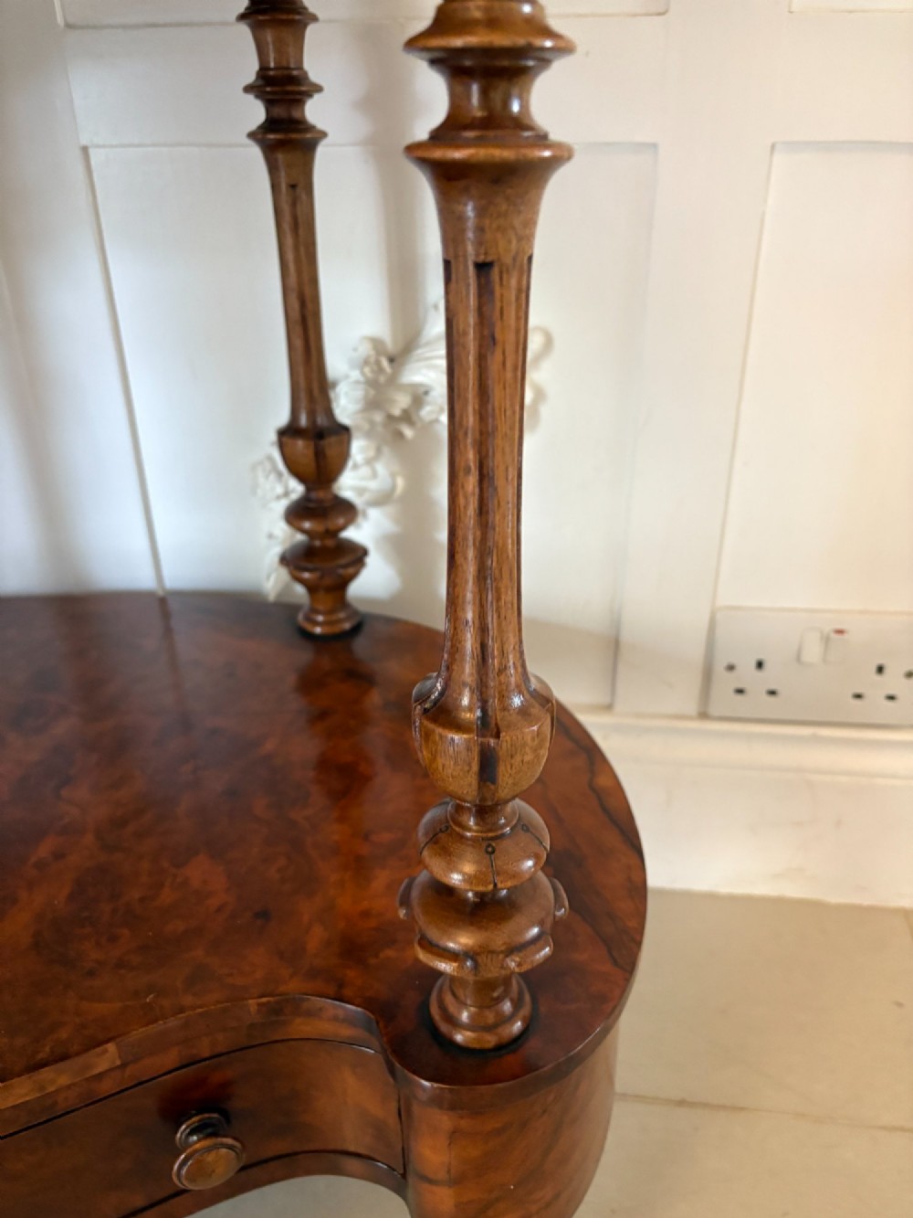 A Victorian burr walnut three-tier serpentine-shaped whatnot featuring turned corner supports, a pierced brass gallery rim, a single bottom drawer, and brass castors. View X