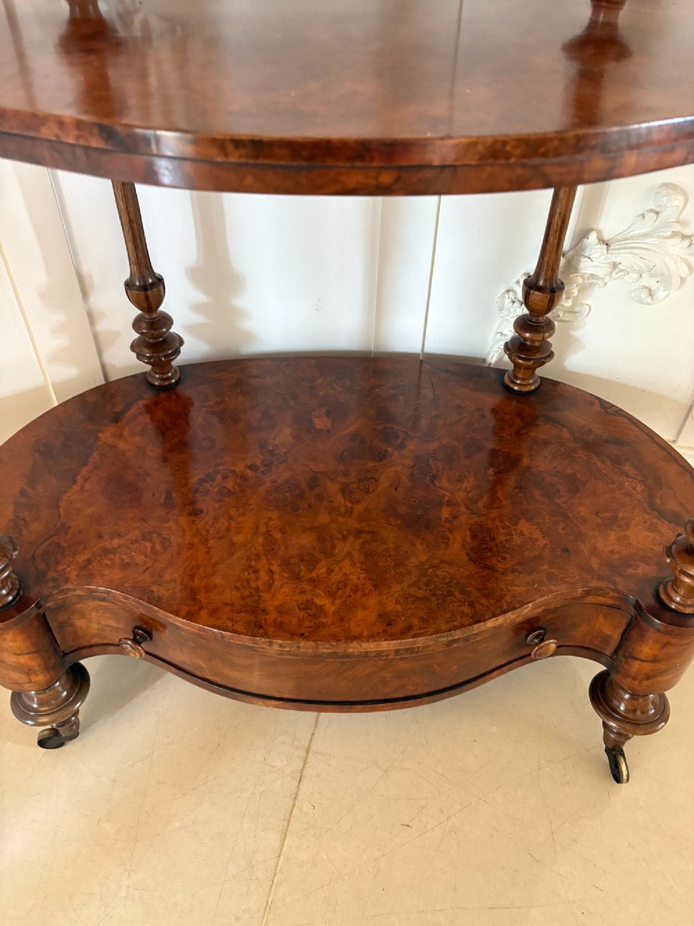 A Victorian burr walnut three-tier serpentine-shaped whatnot featuring turned corner supports, a pierced brass gallery rim, a single bottom drawer, and brass castors. View XIII