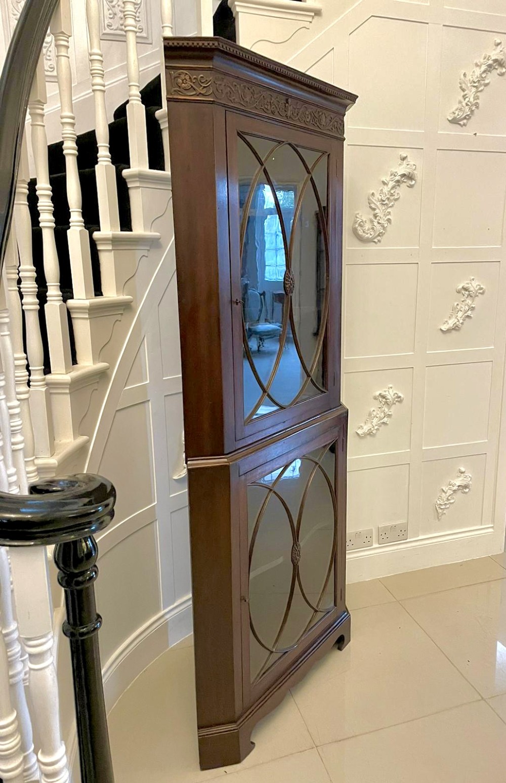 A tall mahogany corner cabinet with two astragal glazed doors featuring curved oval tracery and a carved foliate frieze. View V