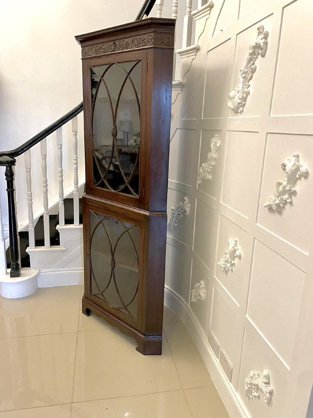 A tall mahogany corner cabinet with two astragal glazed doors featuring curved oval tracery and a carved foliate frieze. View VII