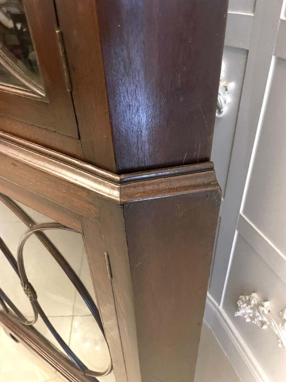 A tall mahogany corner cabinet with two astragal glazed doors featuring curved oval tracery and a carved foliate frieze. View VIII