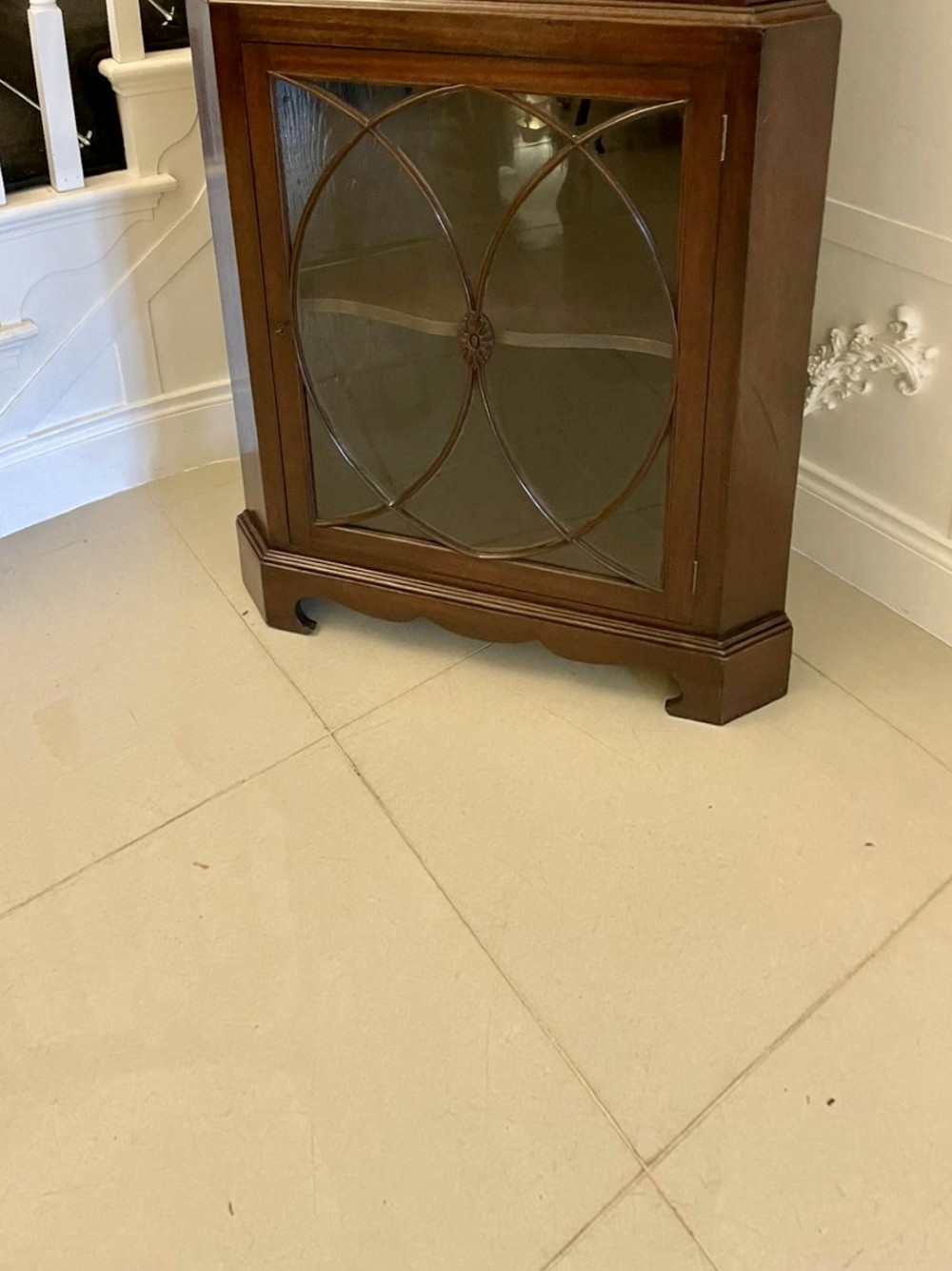 A tall mahogany corner cabinet with two astragal glazed doors featuring curved oval tracery and a carved foliate frieze. View IX