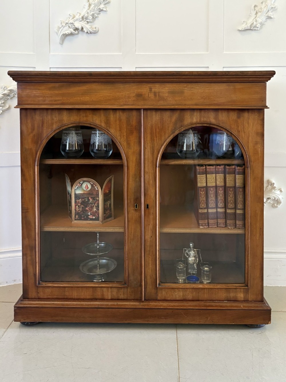 A low Victorian mahogany bookcase featuring two arched glazed doors revealing interior shelving above a plinth base. View V