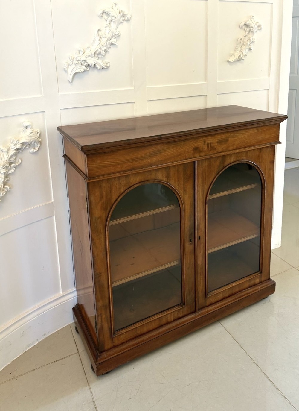 A low Victorian mahogany bookcase featuring two arched glazed doors revealing interior shelving above a plinth base. View VI