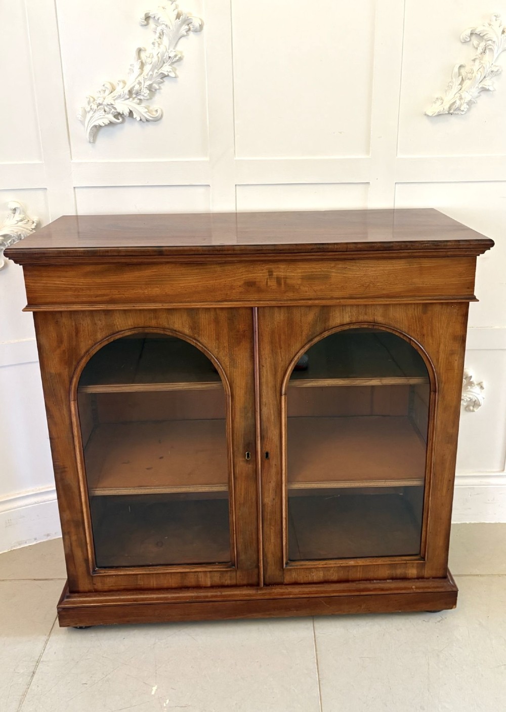 A low Victorian mahogany bookcase featuring two arched glazed doors revealing interior shelving above a plinth base. View VII