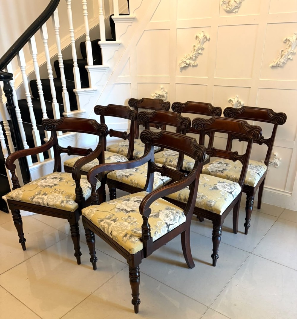 A set of eight Regency mahogany dining chairs comprising six side chairs and two carver armchairs with scroll-carved top rails and turned front legs.