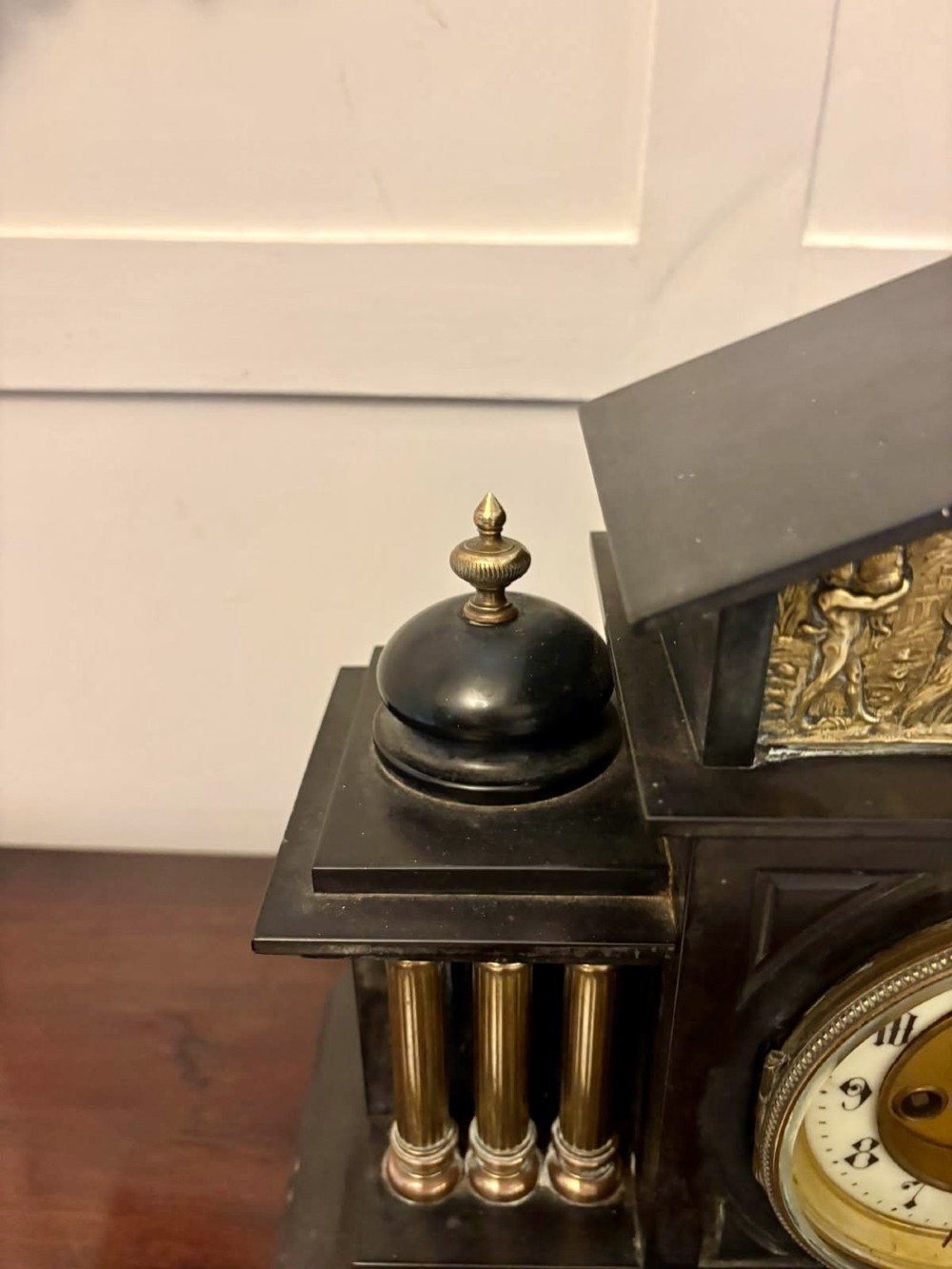 An architectural black marble mantel clock featuring gilt brass columns, a relief frieze panel depicting classical figures, and a round dial with Arabic numerals. View VI