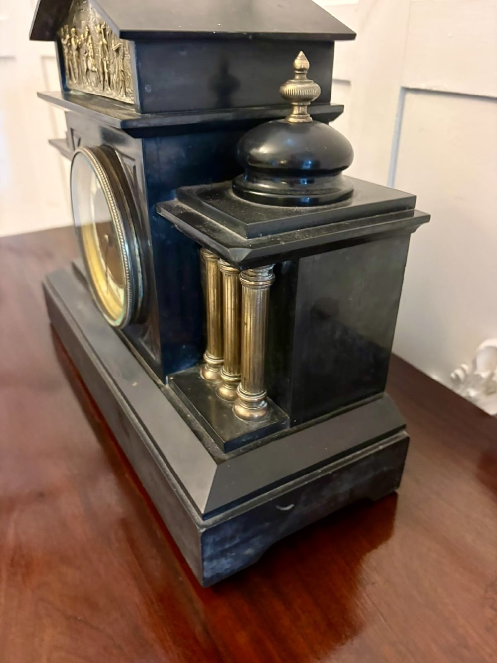 An architectural black marble mantel clock featuring gilt brass columns, a relief frieze panel depicting classical figures, and a round dial with Arabic numerals. View X