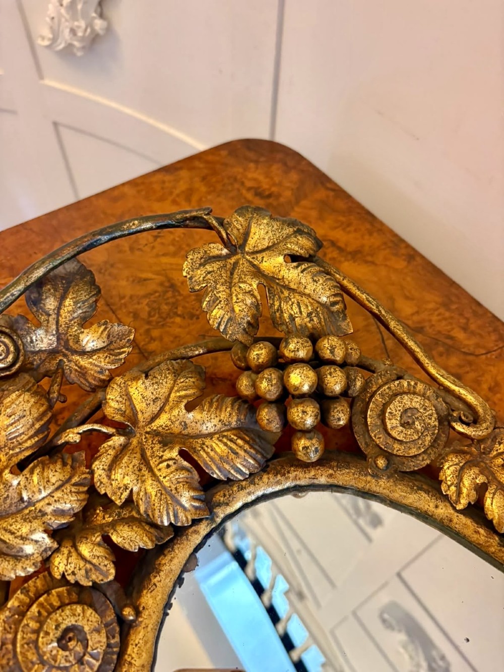 An oval gilt metal tray featuring a central mirror panel surrounded by an ornate border of sculpted grapevines, leaves, and grape clusters. View VI