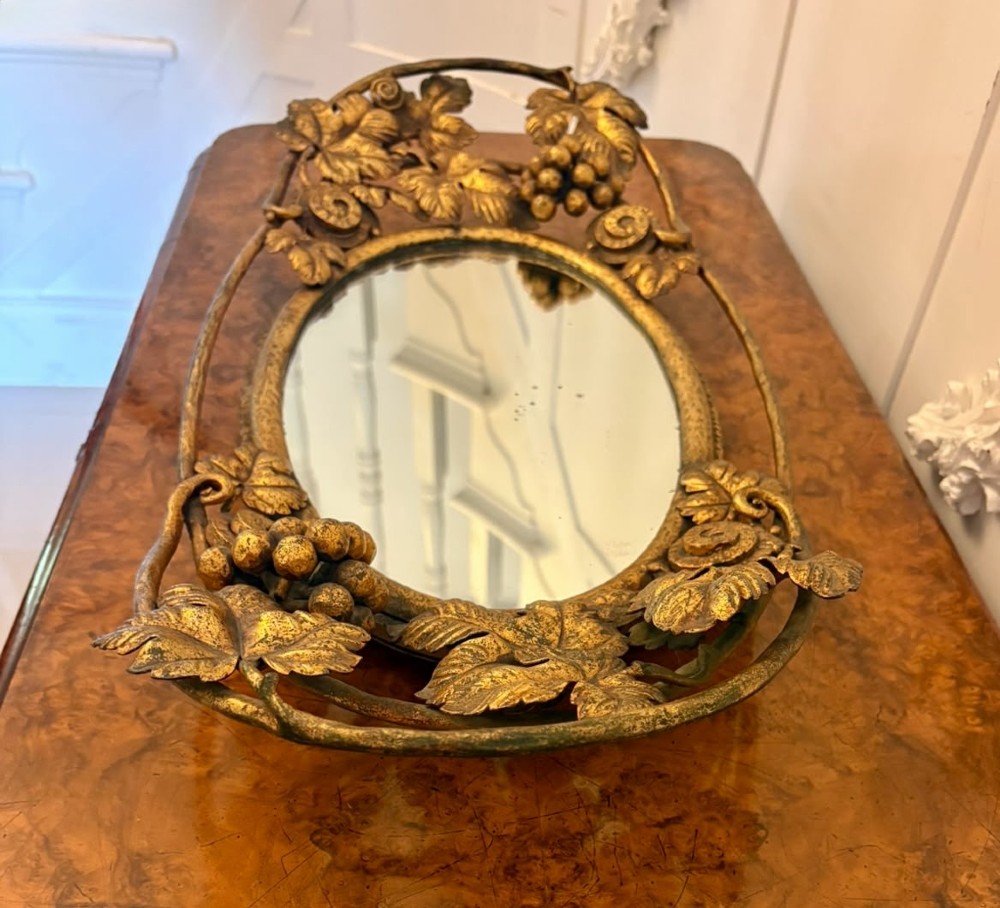 An oval gilt metal tray featuring a central mirror panel surrounded by an ornate border of sculpted grapevines, leaves, and grape clusters. View X