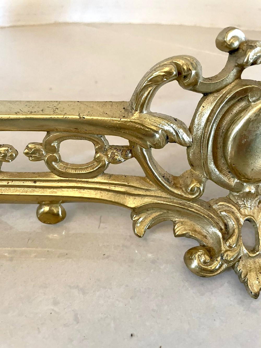An ornate French Rococo style gilded brass extending fireplace fender with intricate scroll ends and an adjustable central bar. View V
