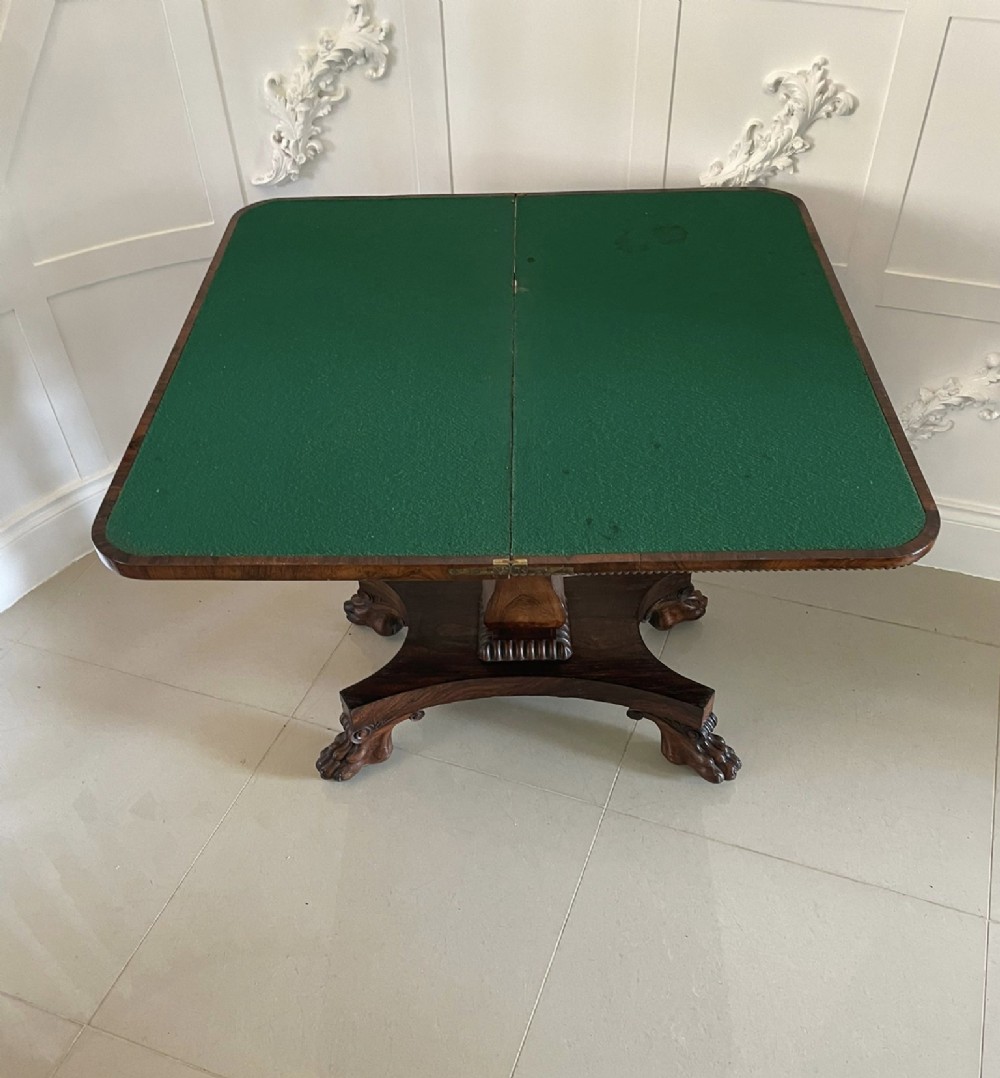 A William IV dark rosewood fold-over card table featuring a gadrooned top edge, scroll carvings, a central pedestal column, and a plinth base on carved claw feet. View VII