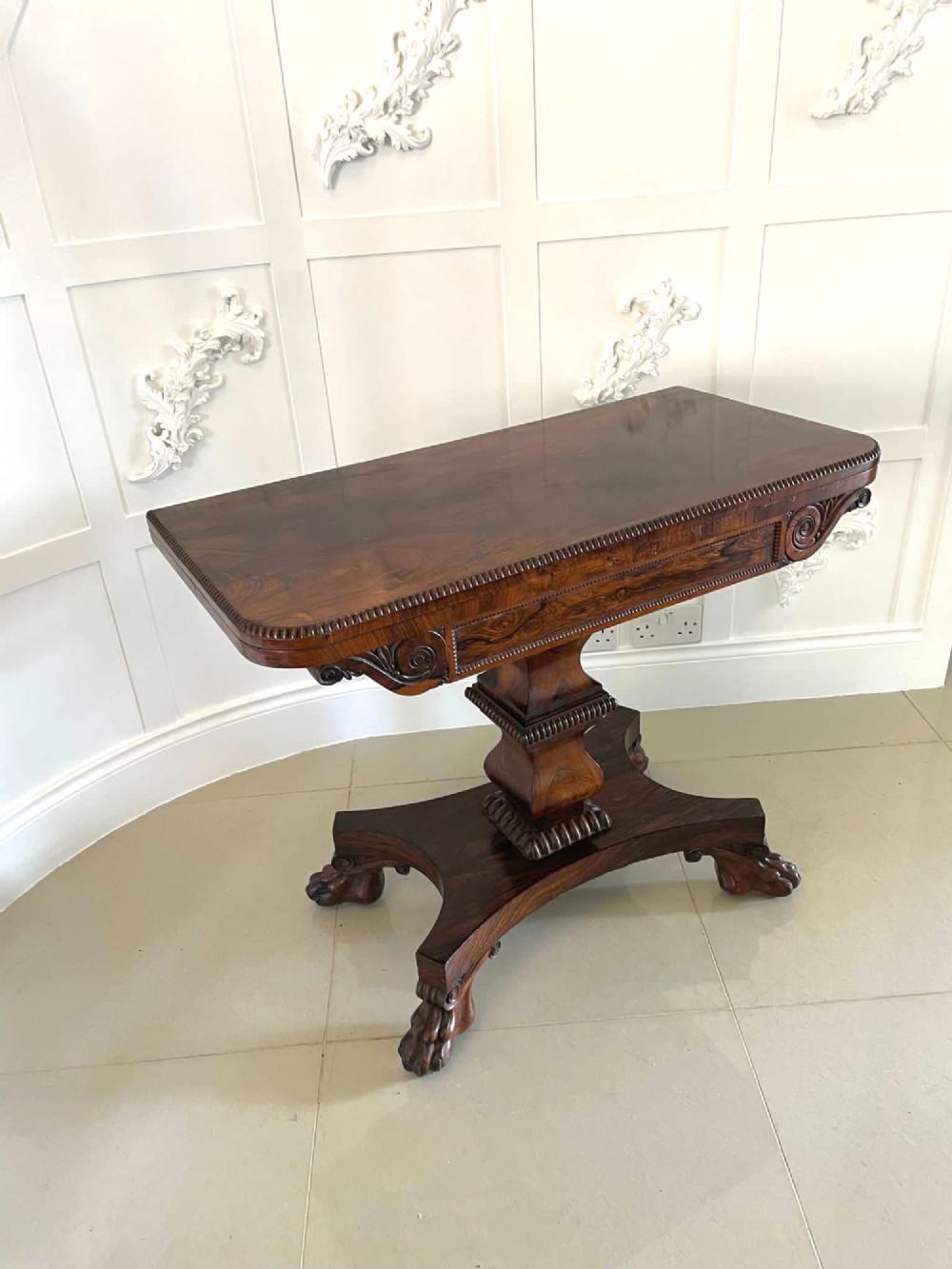 A William IV dark rosewood fold-over card table featuring a gadrooned top edge, scroll carvings, a central pedestal column, and a plinth base on carved claw feet. View VIII