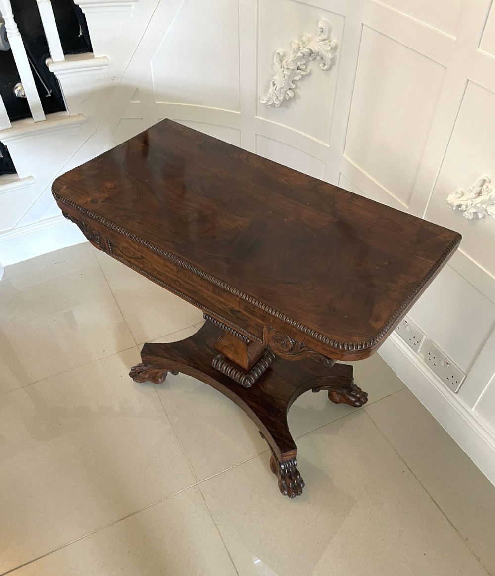 A William IV dark rosewood fold-over card table featuring a gadrooned top edge, scroll carvings, a central pedestal column, and a plinth base on carved claw feet. View XI
