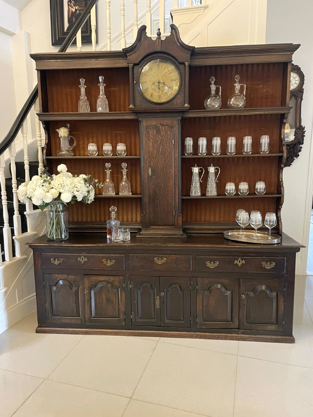 An eighteenth-century dark oak George III dresser featuring an upper shelf rack with an integrated central longcase clock over a base with three drawers and six arched panel cupboard doors. View II