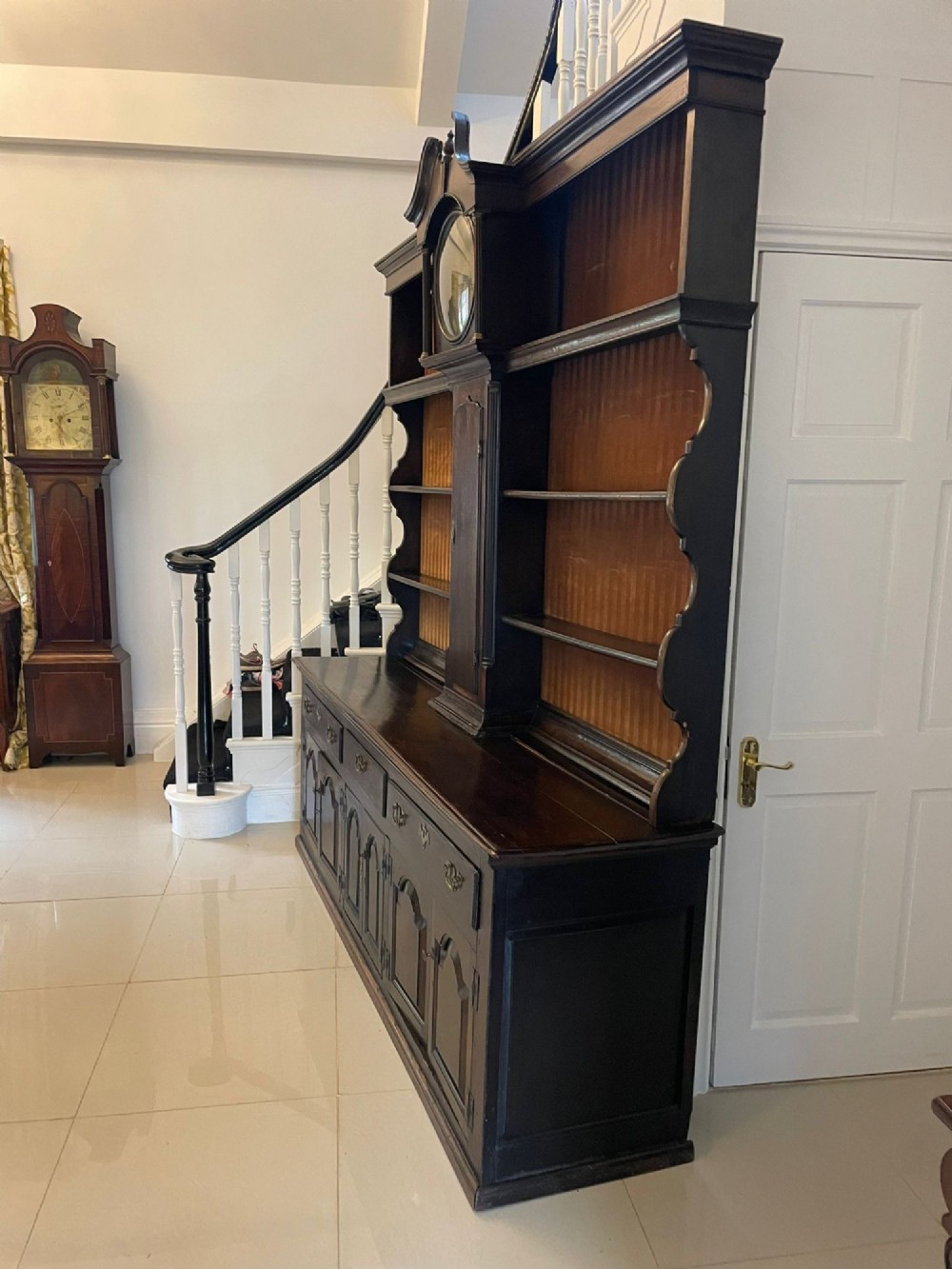 An eighteenth-century dark oak George III dresser featuring an upper shelf rack with an integrated central longcase clock over a base with three drawers and six arched panel cupboard doors. View VI