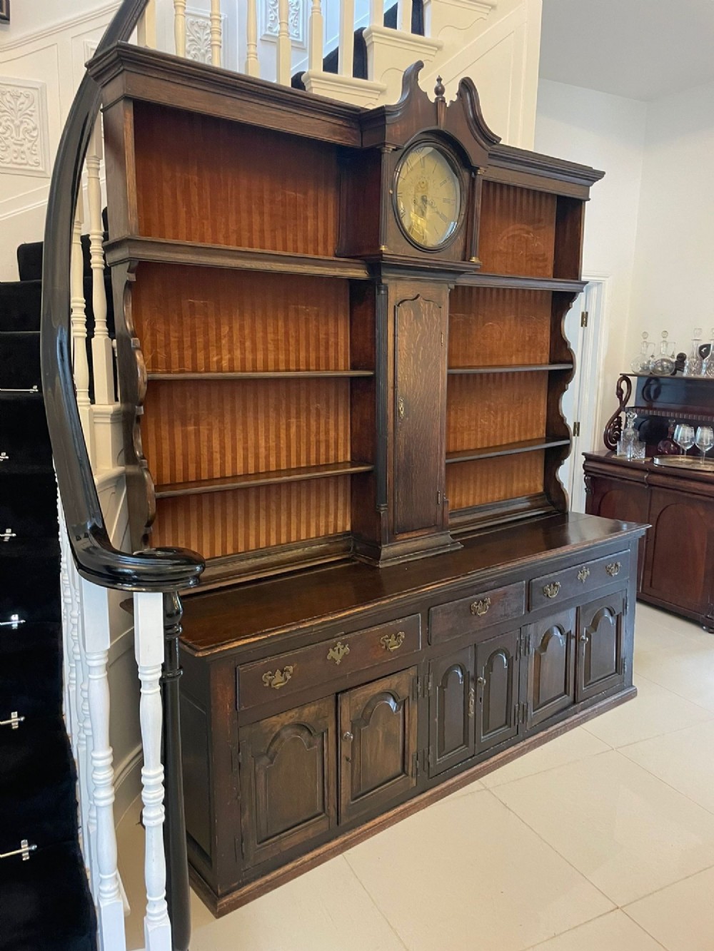 An eighteenth-century dark oak George III dresser featuring an upper shelf rack with an integrated central longcase clock over a base with three drawers and six arched panel cupboard doors. View VII
