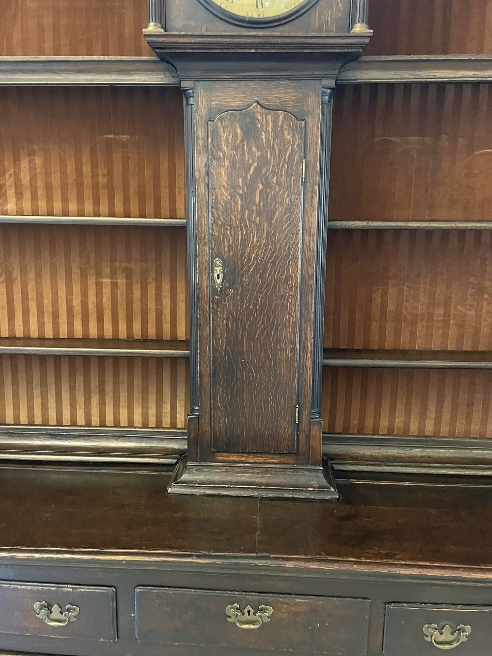 An eighteenth-century dark oak George III dresser featuring an upper shelf rack with an integrated central longcase clock over a base with three drawers and six arched panel cupboard doors. View XIII