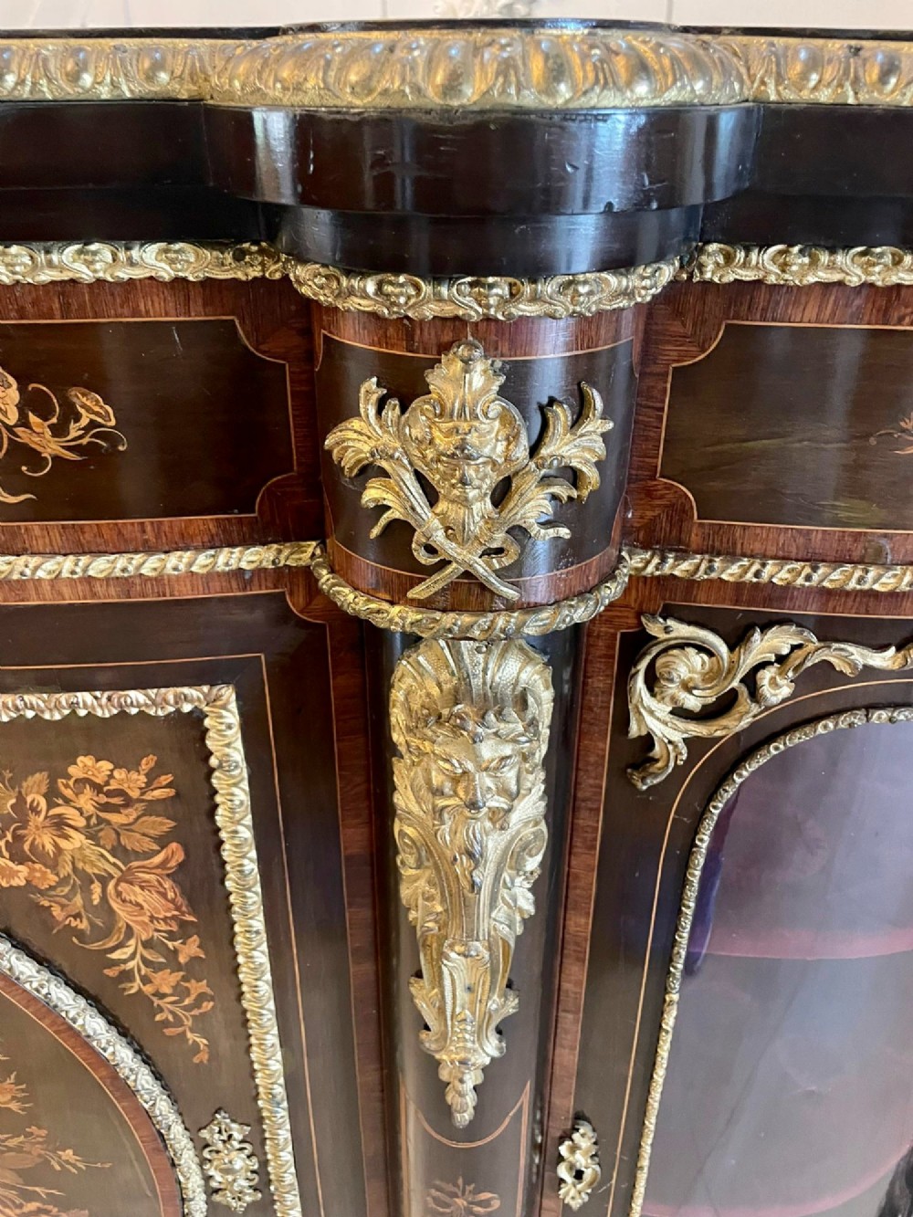 A dark wood Victorian serpentine credenza with floral marquetry inlay, gilt ormolu mounts, and two curved glass display doors. View V