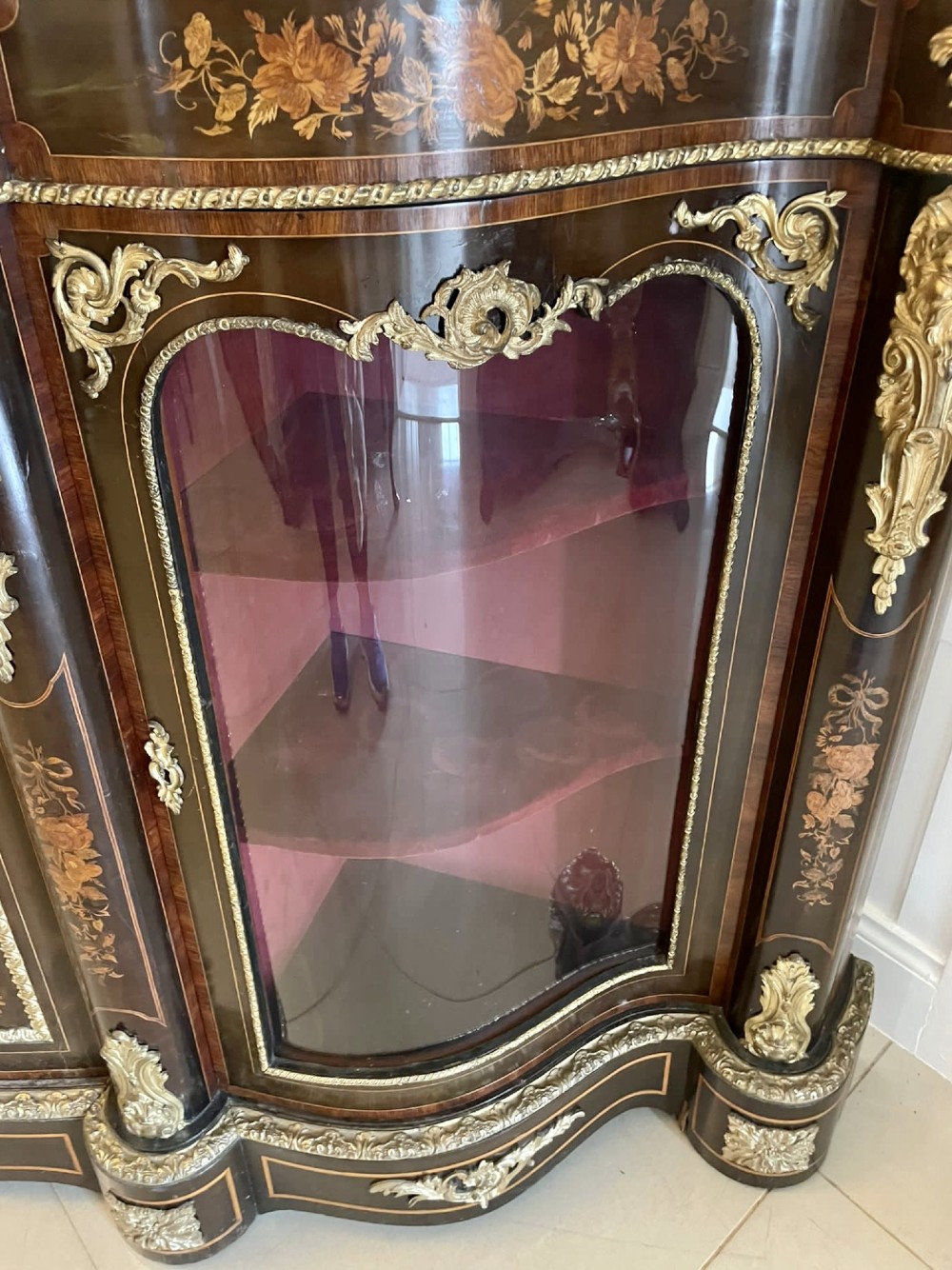A dark wood Victorian serpentine credenza with floral marquetry inlay, gilt ormolu mounts, and two curved glass display doors. View VI