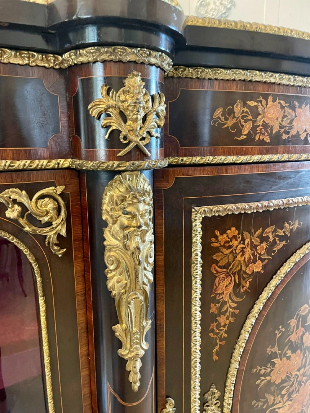 A dark wood Victorian serpentine credenza with floral marquetry inlay, gilt ormolu mounts, and two curved glass display doors. View X