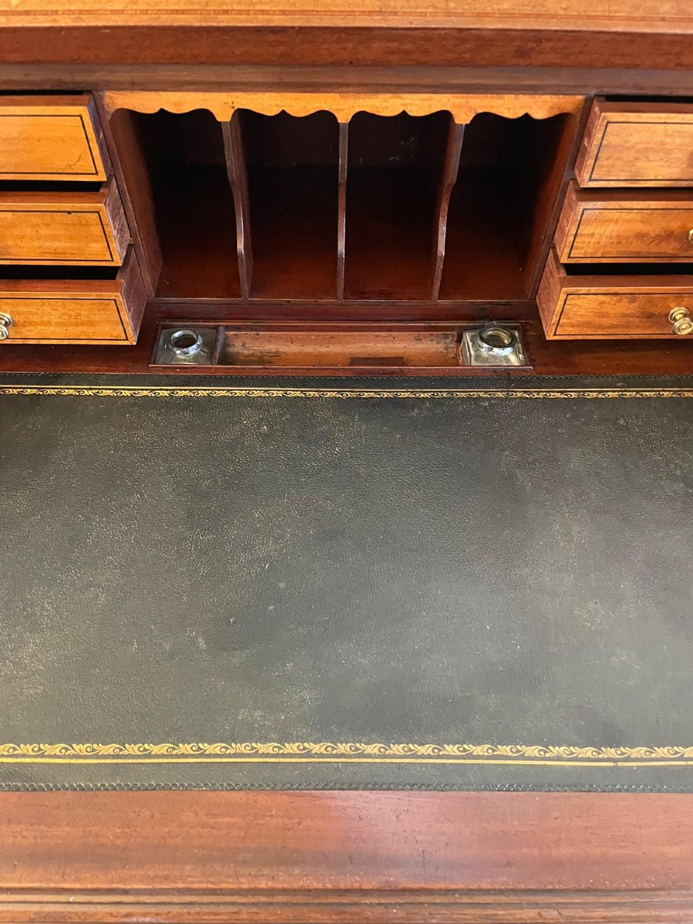 An Edwardian mahogany cylinder writing desk featuring satinwood inlay, brass gallery top rail, and tapered square legs. View V
