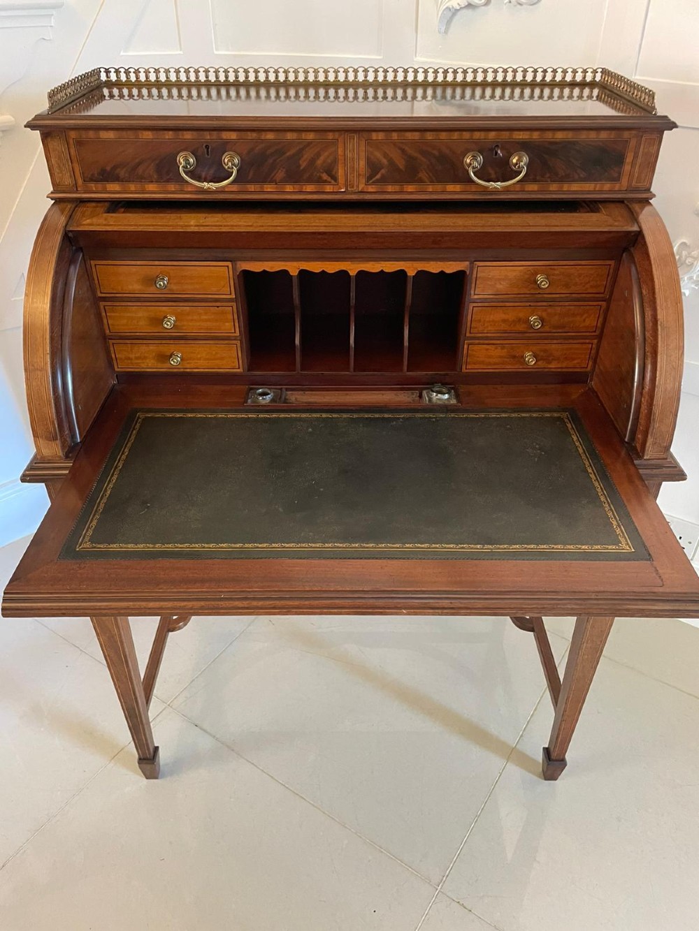 An Edwardian mahogany cylinder writing desk featuring satinwood inlay, brass gallery top rail, and tapered square legs. View VII