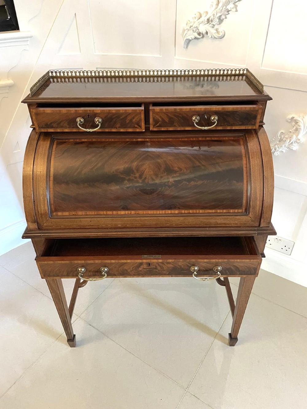 An Edwardian mahogany cylinder writing desk featuring satinwood inlay, brass gallery top rail, and tapered square legs. View XII