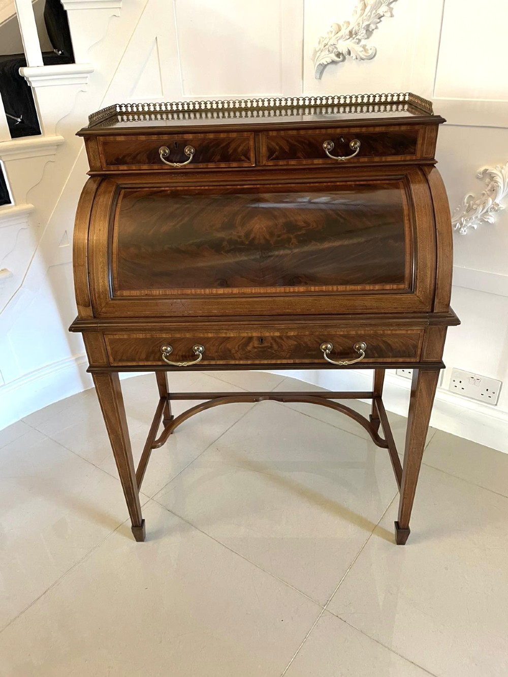 An Edwardian mahogany cylinder writing desk featuring satinwood inlay, brass gallery top rail, and tapered square legs. View XV