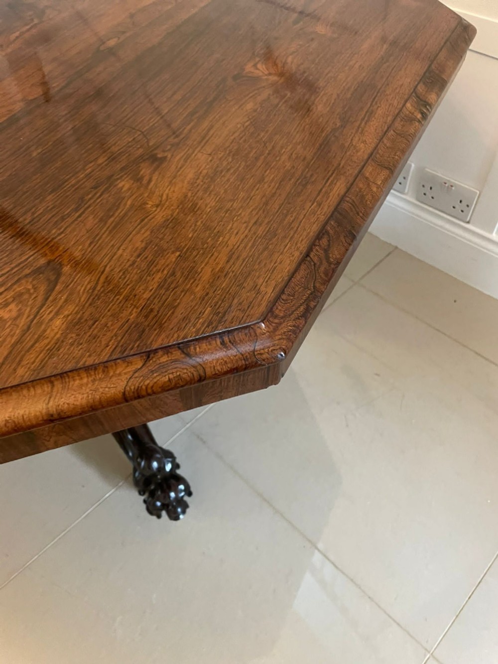 An Early Victorian octagonal rosewood tilt-top centre table with a highly figured grain surface resting on a carved pedestal base with scroll feet. View II